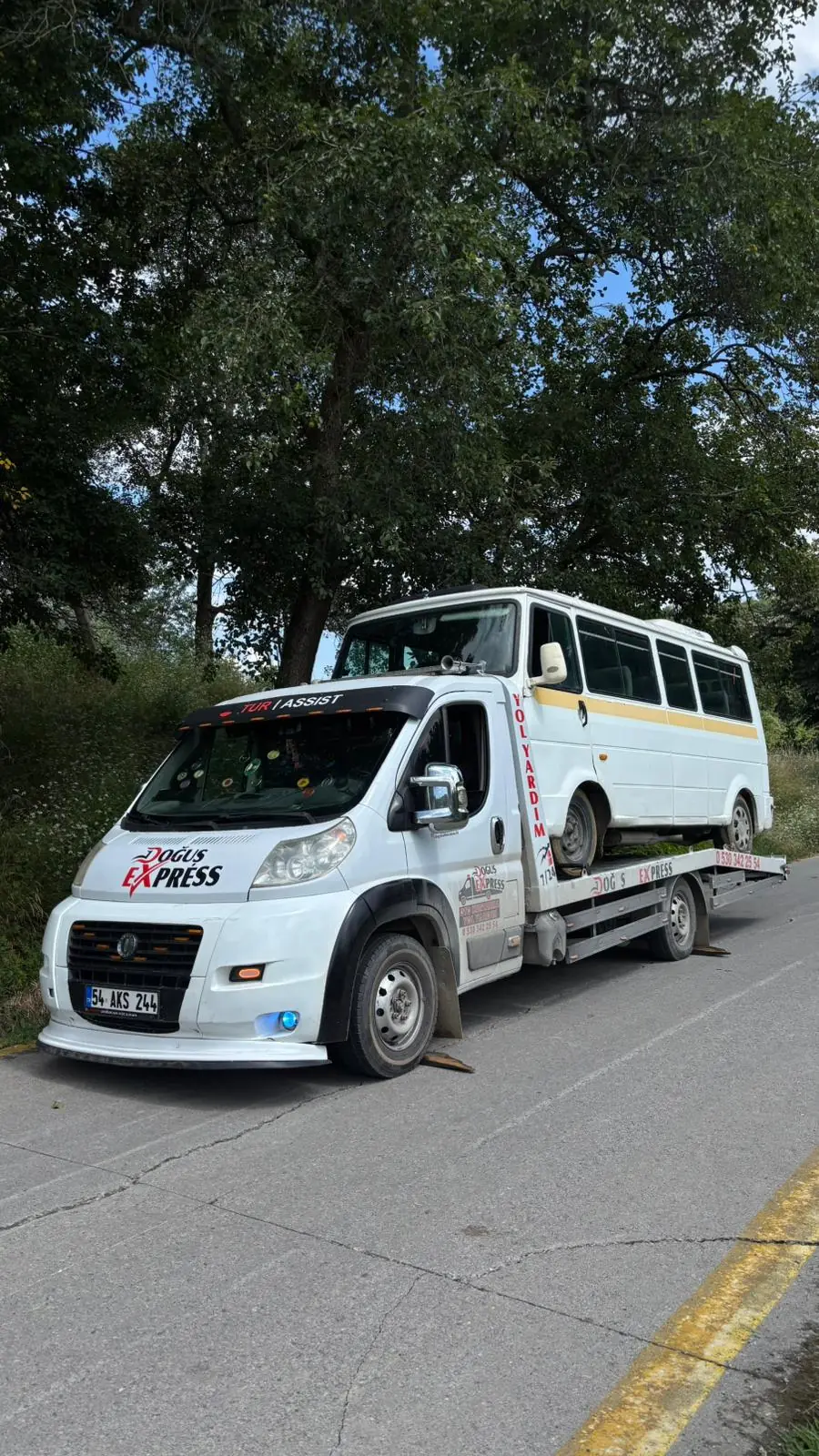 Ağaçlık yol kenarında arızalı minibüsü taşıyan platformlu çekici